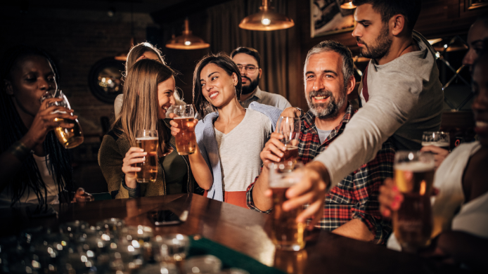 Grupo de personas disfrutando de una jornada de tardeo en un bar, brindando con cervezas y bebidas en un ambiente distendido y social, reflejando la creciente tendencia del ocio vespertino en España.