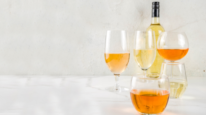 Copas con vino naranja de distintas tonalidades ámbar y doradas junto a una botella de vino blanco sobre una mesa clara.