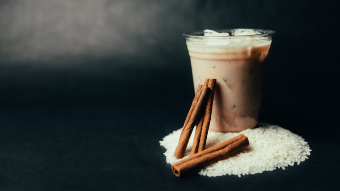 Vaso de horchata fría con canela sobre una base de arroz en fondo oscuro
