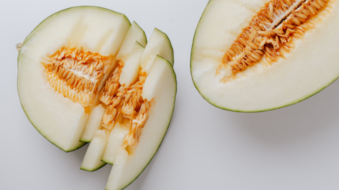 Melón partido por la mitad y cortado en rodajas, con pulpa clara y semillas, como fruta fresca de verano.