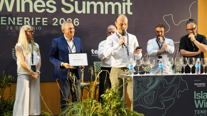 Entrega de un reconocimiento durante Island Wines Summit Tenerife 2026, con varios profesionales sobre el escenario y una mesa de cata con copas de vino.