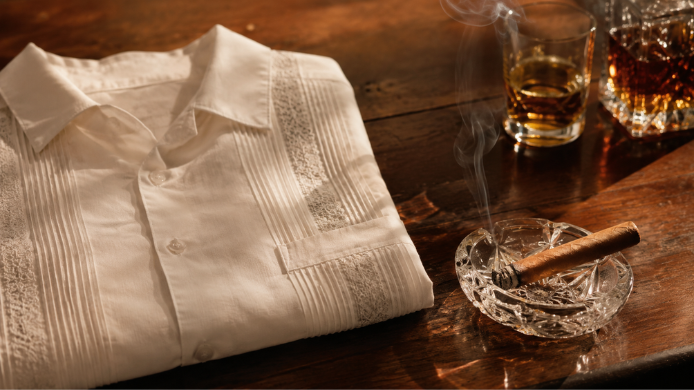 Habano encendido junto a una guayabera blanca sobre una mesa de madera