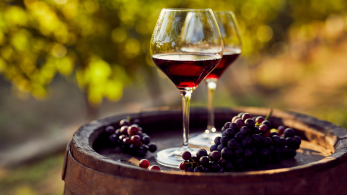 Copas de vino tinto y blanco sobre un barril junto a racimos de uva, en referencia a la nueva categoría de vinos de menor graduación alcohólica en Chile.