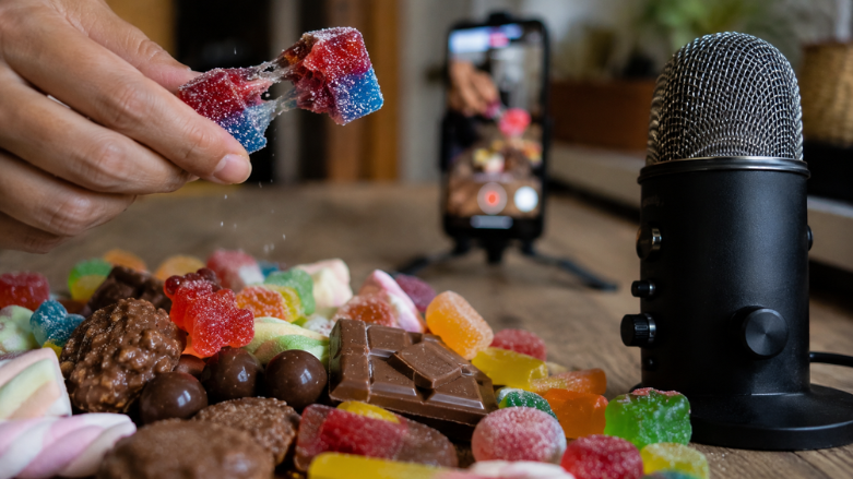 Mano estirando una chuche frente a un micrófono y un móvil mientras se graba un vídeo ASMR de comida