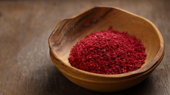 Primer plano de zumaque molido de color rojo intenso servido en un cuenco de madera sobre una superficie oscura, ingrediente tradicional de la cocina de Oriente Medio.
