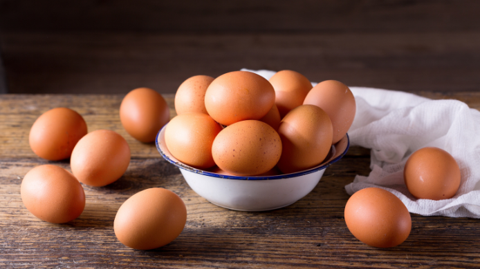 Huevos frescos colocados en un cuenco sobre una mesa de madera, una imagen que refleja la importancia de conservar correctamente este alimento durante los meses de verano para garantizar su calidad y seguridad alimentaria.