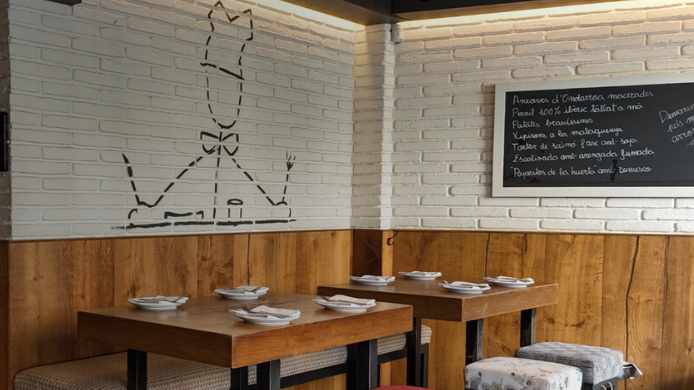 Interior de un restaurante de tapas con mesas de madera, pared de ladrillo blanco y un dibujo minimalista inspirado en el nombre Paco Meralgo.