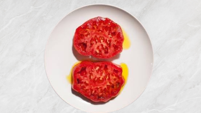 Dos mitades de tomate maduro con aceite de oliva en un plato blanco
