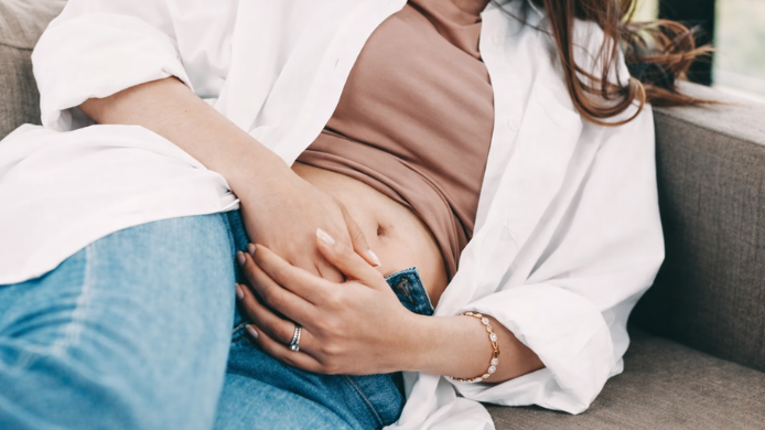 Mujer con pantalón desabrochado por sensación de tripa hinchada o hinchazón abdominal