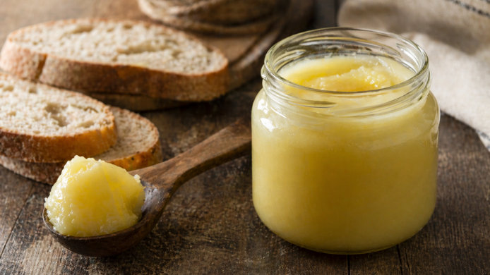 Tarro de manteca de vaca sobre mesa rústica con pan artesanal y cuchara de madera en ambiente tradicional