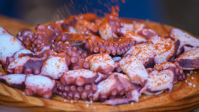 Pulpo á feira servido en plato de madera con pimentón, sal gruesa y aceite de oliva