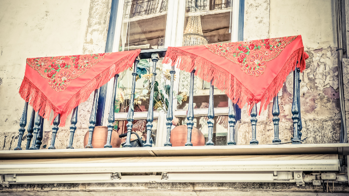 Balcón tradicional de Madrid decorado con mantones de Manila rojos durante las verbenas de agosto.