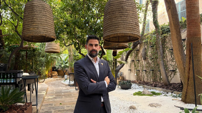 Retrato de Roberto López con traje oscuro y los brazos cruzados en el jardín del restaurante Fera, en Palma de Mallorca.