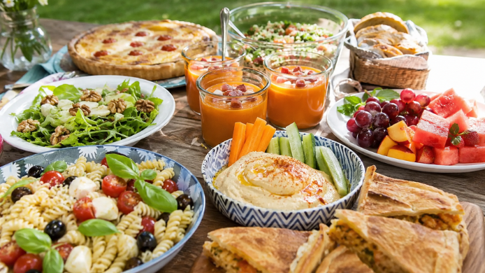 Mesa de verano al aire libre con salmorejo, ensalada de pasta, hummus, fruta fresca, empanada y recetas fáciles para compartir.