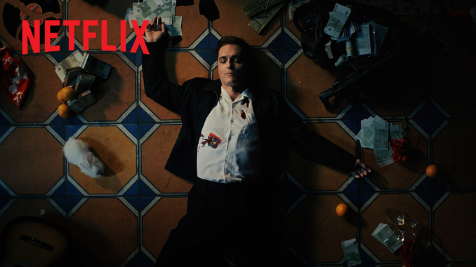 Imagen promocional de la serie Berlín de Netflix con el protagonista tumbado sobre un suelo de baldosas andaluzas, rodeado de billetes y objetos, en una escena de estética cinematográfica.