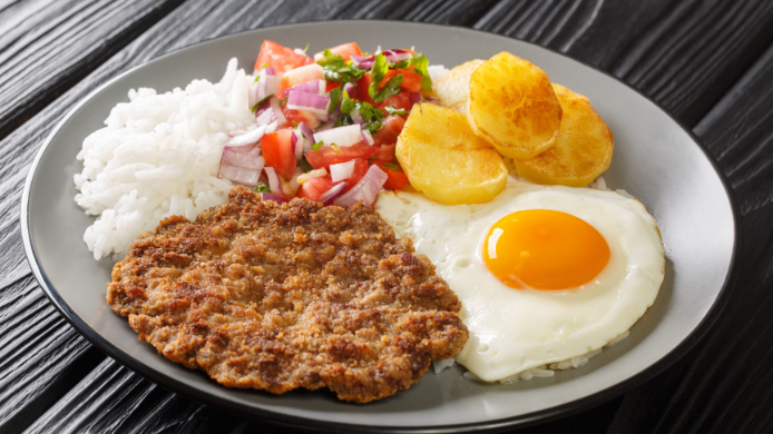 Silpancho cochabambino con carne empanada, arroz, patatas doradas, huevo frito y ensalada de tomate y cebolla.