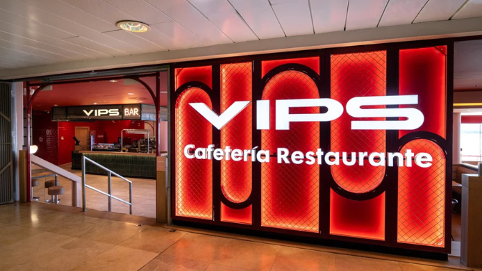 Entrada de un restaurante VIPS en un aeropuerto, con rótulo rojo iluminado, pantallas promocionales y zona interior con mesas para viajeros.
