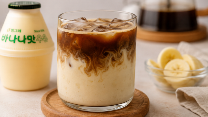 Banana Milk Coffee con espresso, leche de plátano y hielo servido en un vaso transparente, acompañado de rodajas de plátano.