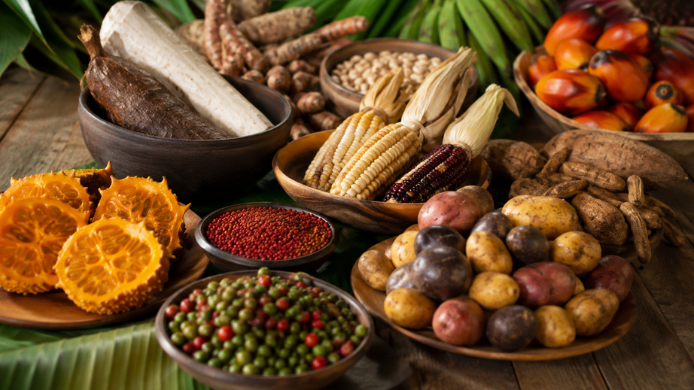 Selección de productos vernáculos colombianos, como maíz, yuca, papas, chontaduro y plátano, dispuestos sobre una mesa de madera.