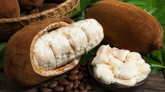 Fruto de copoazú abierto con pulpa blanca, semillas y hojas verdes sobre una mesa de madera