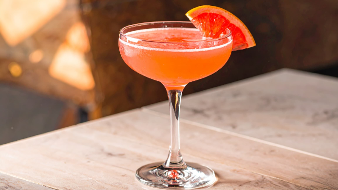 Cóctel Siesta servido en copa elegante con garnish de pomelo rojo, una combinación de tequila, Campari y cítricos con perfil fresco y veraniego.