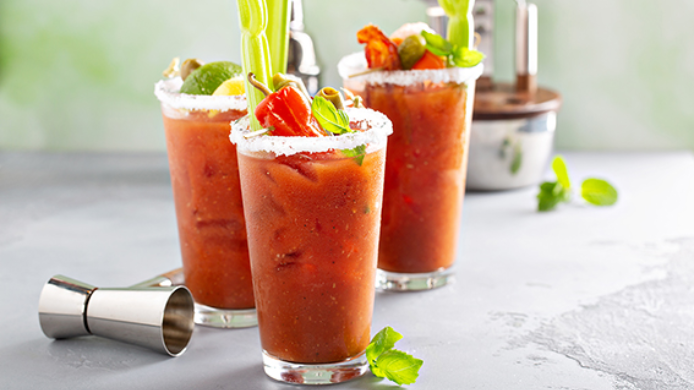 Vasos de bebida salada de tomate con hielo, borde de sal, apio, aceitunas y hierbas frescas