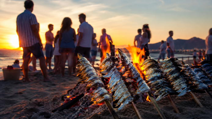 Sardinas asándose junto a una hoguera en la playa durante la celebración de la noche de San Juan, una de las tradiciones gastronómicas más populares del inicio del verano en España.