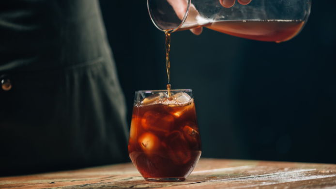 café cold brew desde una jarra de vidrio hacia un vaso con cubos de hielo