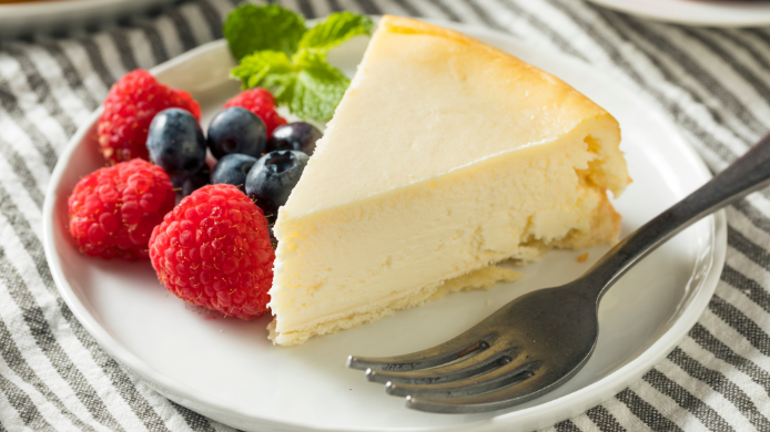 Porción de tarta de queso New York Cheesecake con frutos rojos frescos y menta en plato de postre.