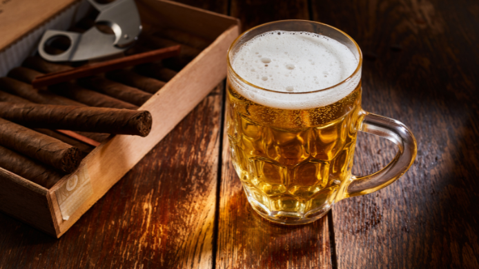 Jarra de cerveza junto a una caja de Habanos y un cortador sobre una mesa de madera