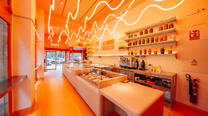 Interior de F de Focaccia en Madrid, un moderno local especializado en focaccias gourmet artesanas, con diseño contemporáneo dominado por tonos naranjas y una barra abierta donde se preparan los pedidos al momento.