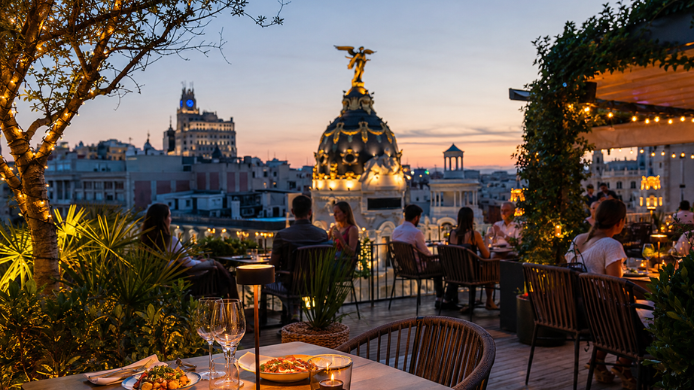 Terraza de restaurante en Madrid al atardecer con mesas servidas, luces cálidas y vistas a la Gran Vía