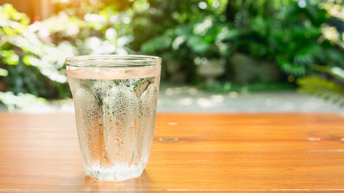 Vaso de agua helada en primer plano con un fondo de jardín verde difuminado.