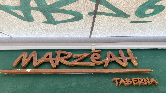 Rótulo de madera de Marzeah Taberna sobre una pared verde en su local de Madrid.