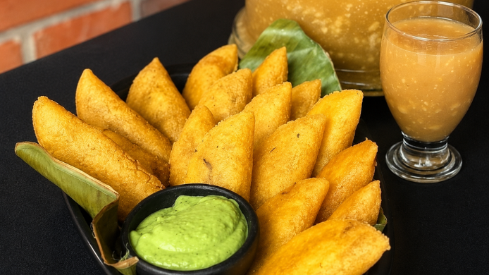Empanadas doradas de maíz acompañadas de salsa verde y una bebida tradicional de maíz servida en vaso 