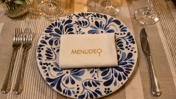 Servilleta bordada con el logo de Menudeo sobre plato decorado en una mesa de restaurante