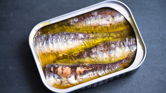 Lata de sardinas en aceite de oliva con pescado entero brillante y textura jugosa sobre fondo oscuro