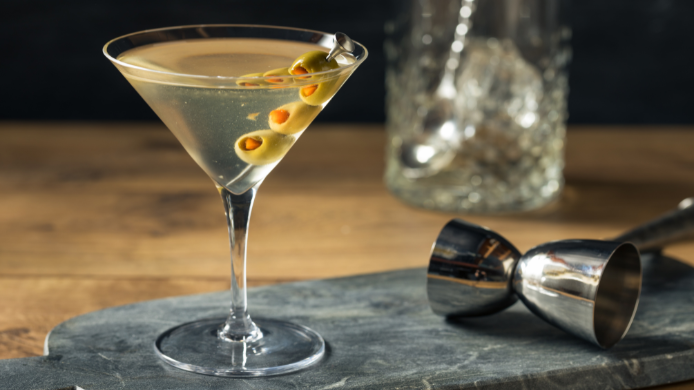 Copa de Dirty Martini con aceitunas verdes servida sobre una barra de coctelería