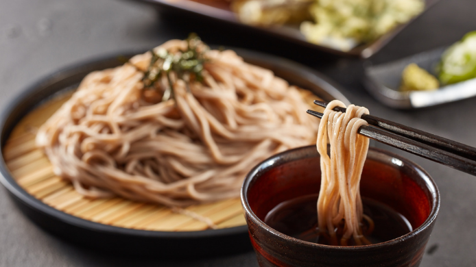 Zaru Soba tradicional japonés servido sobre una bandeja de bambú con salsa tsuyu. Unos palillos sostienen los fideos fríos antes de sumergirlos en el caldo para su degustación.