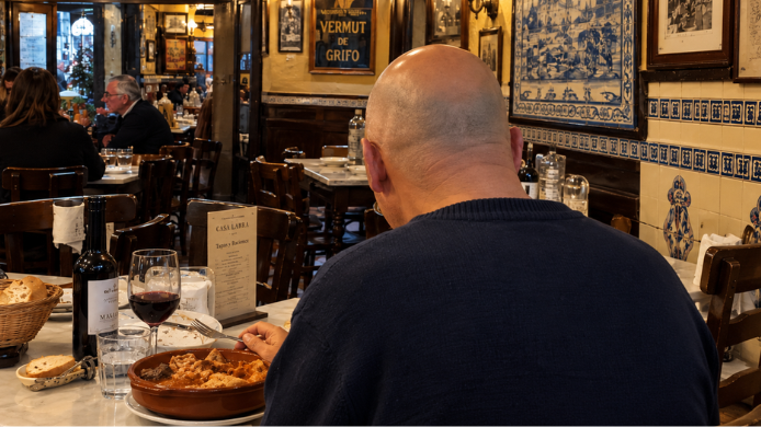 Hombre calvo de espaldas comiendo callos a la madrileña en una taberna tradicional de Madrid