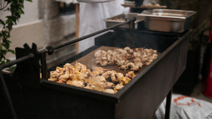 Parrilla con piezas de pollo cocinándose lentamente sobre brasas, una de las tendencias gastronómicas del verano que apuesta por carnes de ave más jugosas, ligeras y versátiles para las barbacoas.