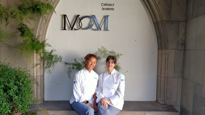Dos cocineras con chaqueta blanca sentadas en la entrada de MOM Culinary Institute
