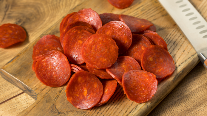 Lonchas de pepperoni sobre una tabla de madera junto a un cuchillo.