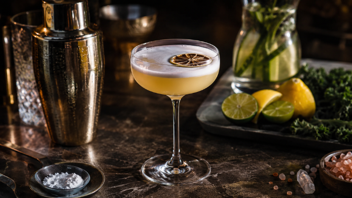 Cóctel cítrico con espuma servido en copa, acompañado de ingredientes asociados a bebidas funcionales como minerales y suplementos en polvo