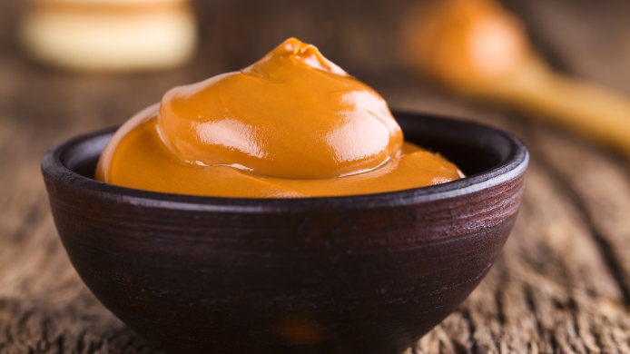 cuenco de arcilla marrón lleno de dulce de leche cremoso sobre una mesa de madera rústic