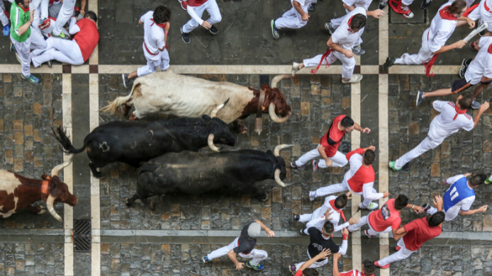 Encierro de San Fermín visto desde arriba, con corredores vestidos de blanco y rojo corriendo junto a varios toros por las calles de Pamplona.