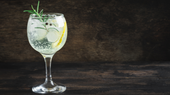 Gin tonic servido en una copa de balón, decorado con una rodaja de lima, abundantes cubitos de hielo y ramitas de romero fresco. Cócteles fáciles