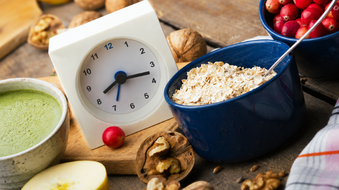 Reloj junto a avena, fruta, frutos secos y matcha, imagen asociada a las tendencias nutricionales actuales como el ayuno intermitente y la alimentación saludable