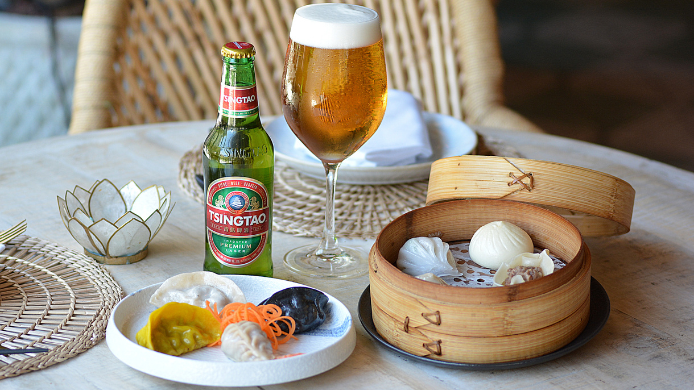 Dim sum servido en cesta de bambú junto a cerveza Tsingtao en una mesa de restaurante