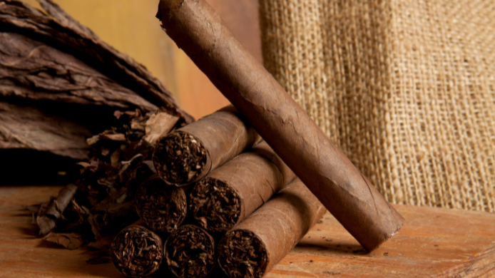Primer plano de varios habanos artesanales elaborados con hojas de tabaco, colocados sobre una superficie de madera junto a hojas curadas, símbolo de la tradición y el arte de la fabricación de puros premium.